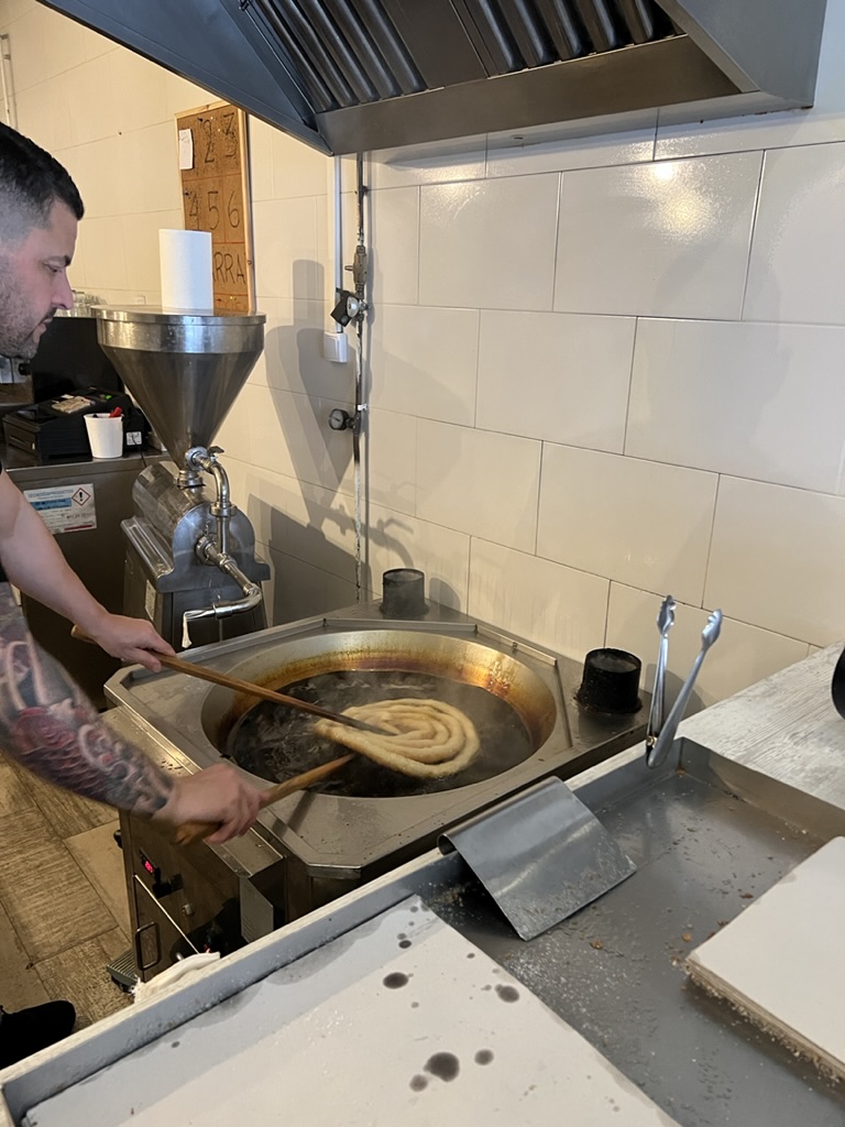 A man fries churros in a spiral pattern over a deep vat of oil