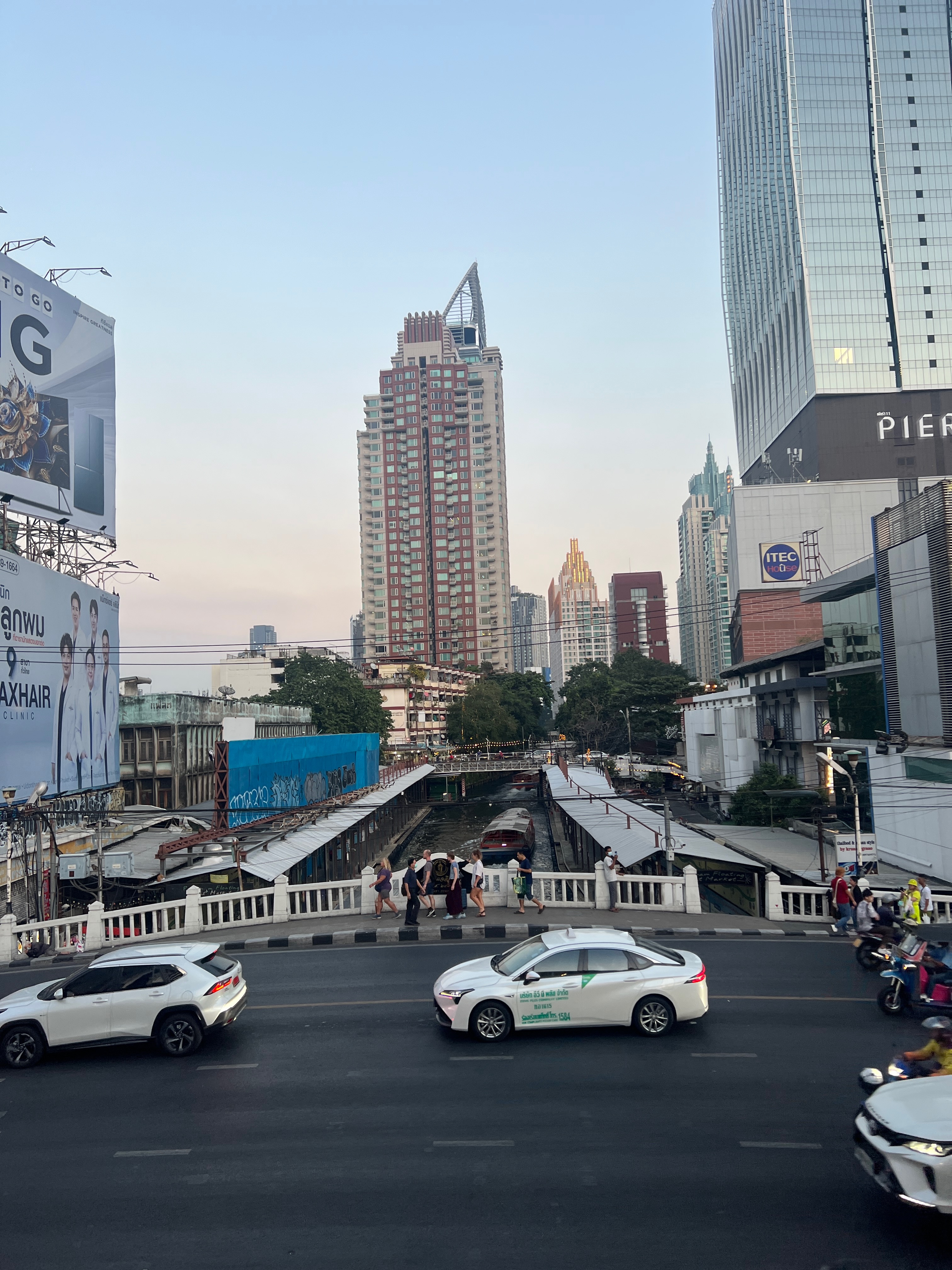 cars pass on the road below, with a skycraper in the background against a sunset-colored sky.