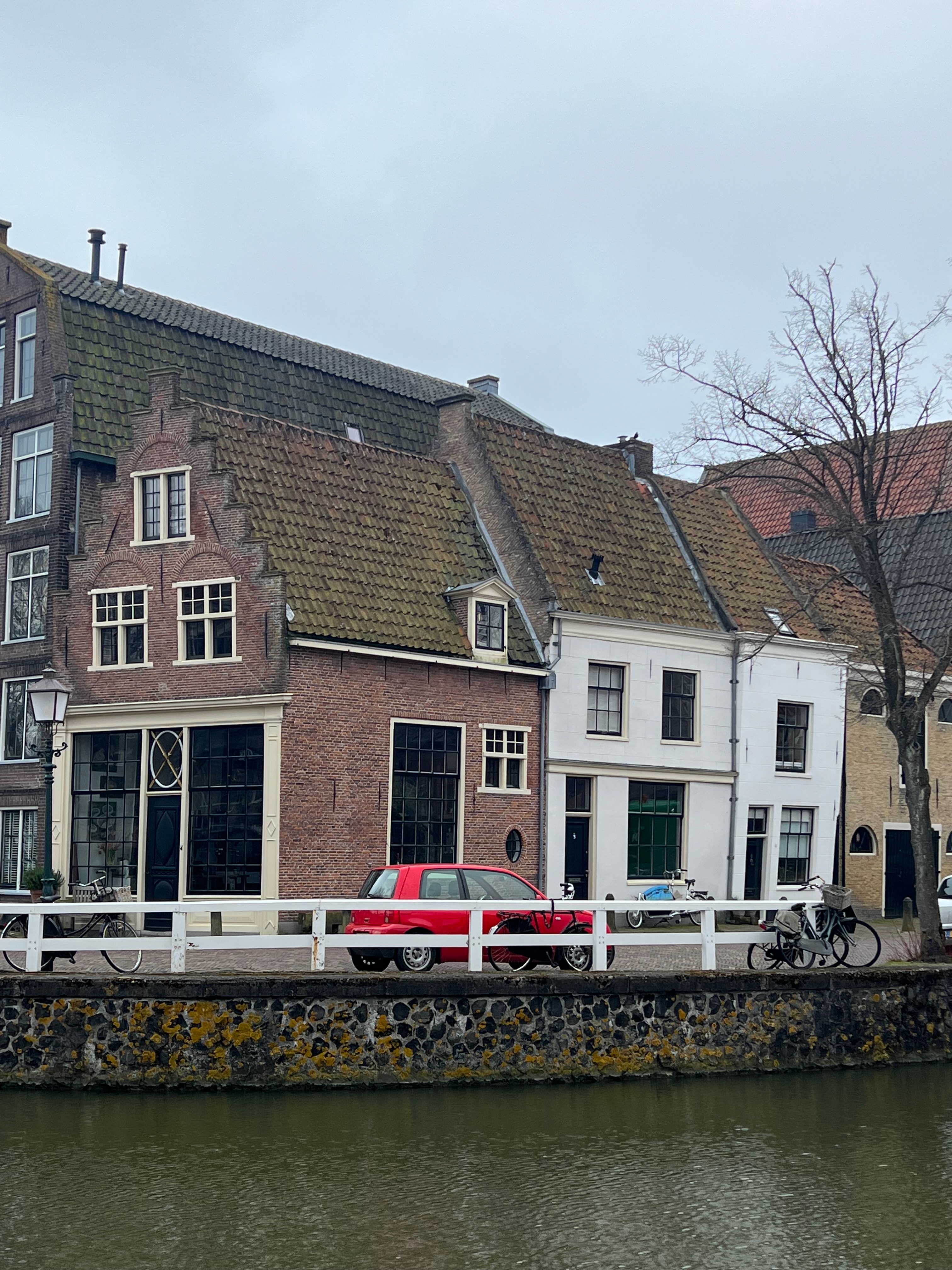 Picture of Hoorn town. A canal in the foreground with a brick 30story building and a red car.